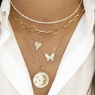 Woman wearing pearl & diamond butterfly necklace layered under yellow gold chain link & diamond necklaces