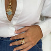 Round stone ring displayed on woman's hand with large charm necklace