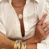 Woman wearing rectangle link necklace with medallion, triple bracelets, and pave rings