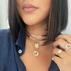 Herringbone necklace paired with yellow gold charm necklaces and rings on woman's neck and hand
