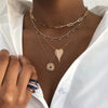 Woman wearing plain heart necklace layered with other gold necklaces and cluster ring