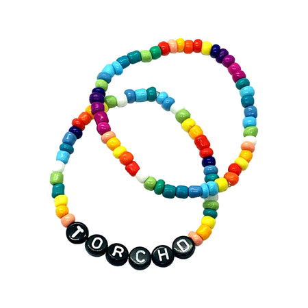 Torch’d Stretch Bracelet Set   Set of 2 rainbow stretch bracelets. One says torchd, the other is plain.  A must have bracelet set honoring celebrity fitness guru Issac Boots benefiting No Kid Hungry. Get torch'd with us & donate today.  Estimate delivery is 3 weeks.  20% of proceeds to No Kid Hungry. view 1
