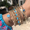 Multi charm bracelet displayed on girl's wrist with yellow gold bead bracelets