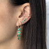 Woman wearing emerald and diamond drop earrings with matching crawlers and yellow gold pave huggie earrings