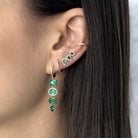 Woman wearing emerald and diamond drop earrings with matching crawlers and yellow gold pave huggie earrings