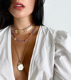 Chain necklace with heart and white enamel charm, layered with rainbow bead necklaces and yellow gold herringbone