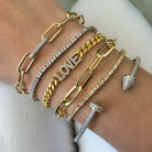 Oval link bracelet displayed on wrist layered next to yellow gold chain link and pave diamond bracelets