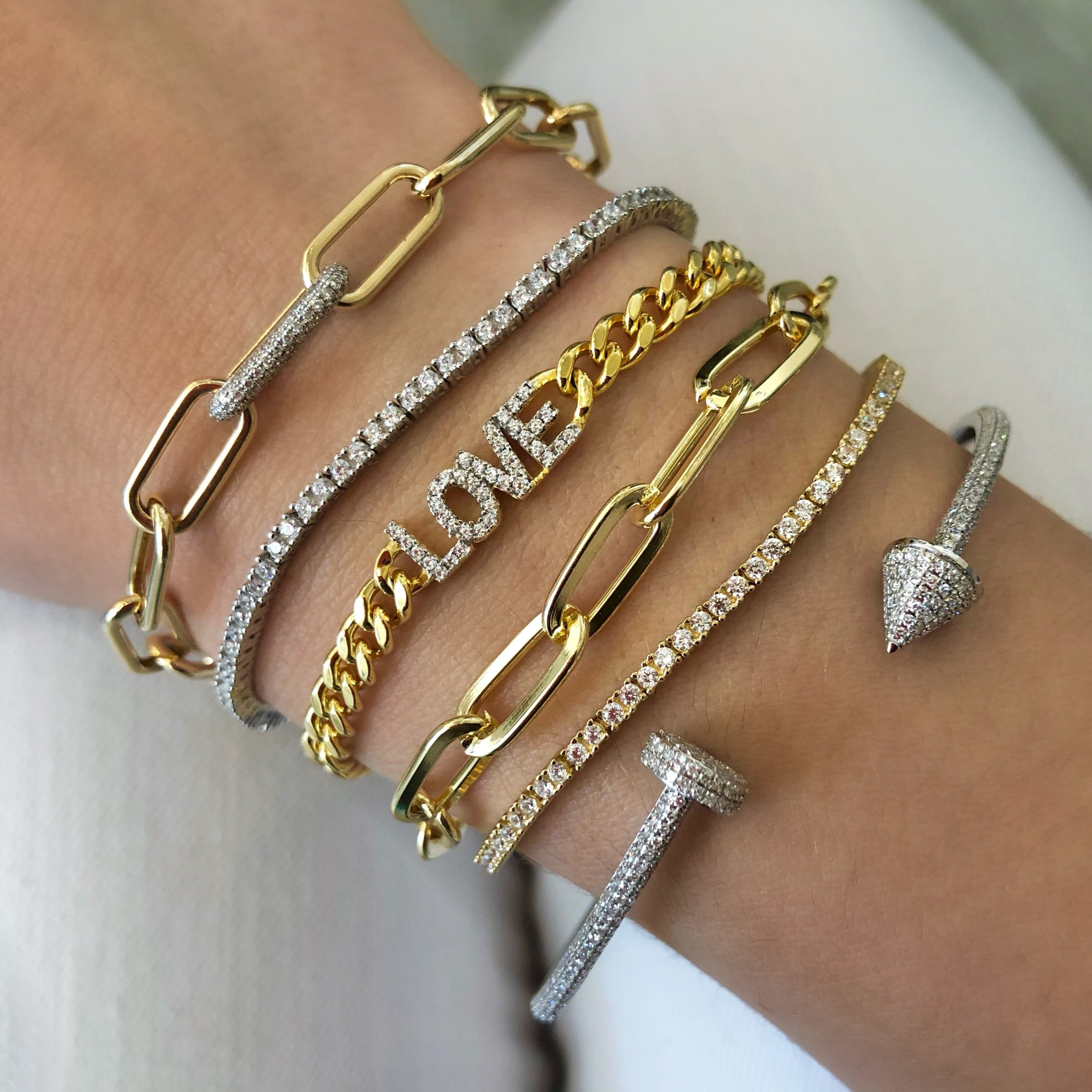 Oval link bracelet displayed on wrist layered next to yellow gold chain link and pave diamond bracelets