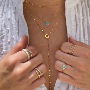 Woman wearing twinkle lariat with layered yellow gold necklaces and yellow gold rings from collection