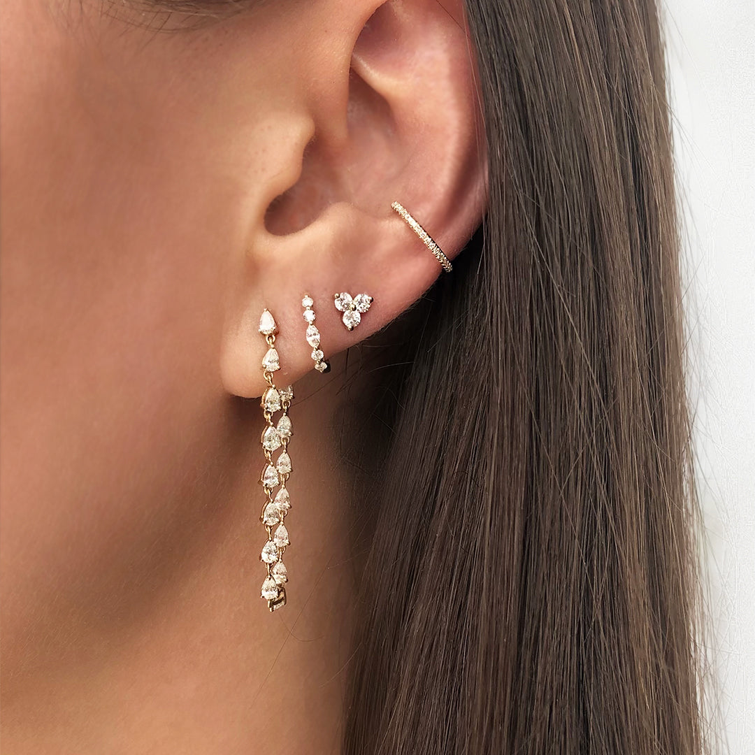Diamond teardrop earrings on woman's ear with diamond huggie, stud, and ear cuff