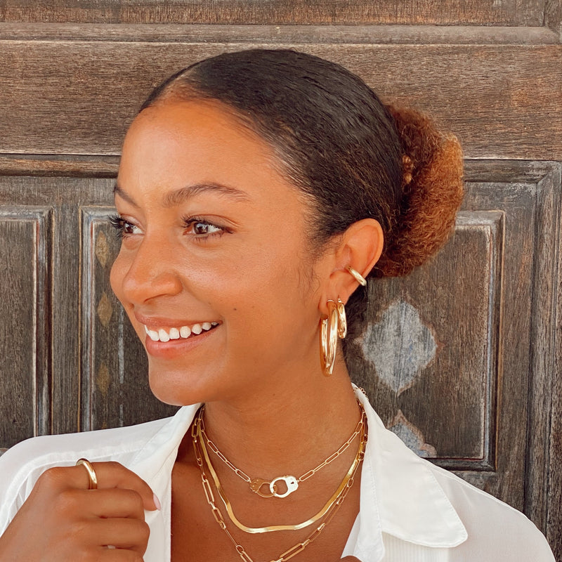Woman wearing small thick hoops with yellow gold chunky jewelry