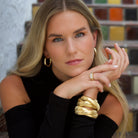 Woman wearing yellow gold plated triple strand bracelet with thick yellow gold hoops and gypsy ring