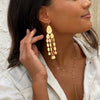 Close up of woman wearing chandelier drop earrings with delicate yellow gold lariat necklace