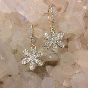 Close up of yellow gold daisy drop earrings against a white crystal background
