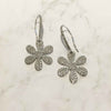 Naturally lit white gold daisy drop earrings against marbled background